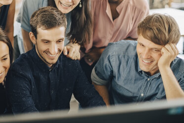 Lächelnde kreative Geschäftsleute, die während einer Besprechung im Büro auf einen Computerbildschirm schauen - MASF10685