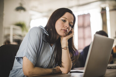 Tensed businesswoman looking at laptop while sitting at desk in creative office - MASF10690