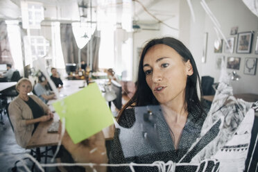 Businesswoman writing on sticky note while explaining colleagues during meeting in creative office - MASF10708