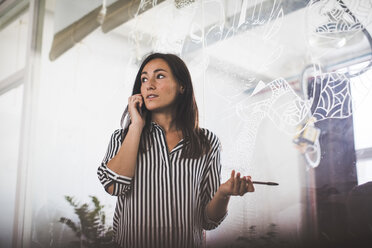 Kreative Geschäftsfrau, die wegschaut, während sie mit einem Mobiltelefon im Sitzungssaal spricht - MASF10722