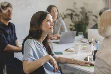 Businesswoman with colleagues listening while sitting in conference room during business meeting - MASF10743