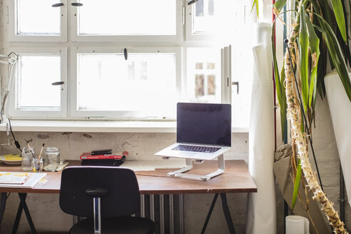 Laptop auf Ständer am Schreibtisch vor dem Fenster im Büro - MASF10753