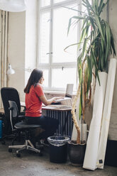 Seitenansicht einer Geschäftsfrau, die einen Laptop am Schreibtisch in einem kreativen Büro benutzt - MASF10757