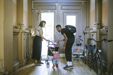 Mother and father looking at daughter pushing baby stroller in corridor of apartment - MASF10775