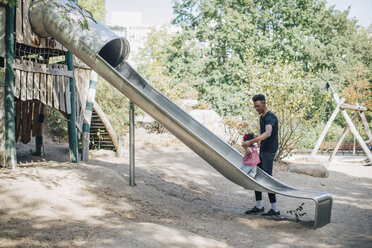 Father holding hands of daughter walking on slide at playground - MASF10782