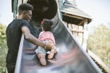 Father supporting daughter crawling up on slide at playground - MASF10786