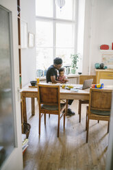 Junger Mann sitzt mit seiner Tochter am Esstisch, gesehen durch eine Tür im Haus - MASF10791