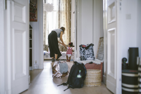 Mutter, die ihrer Tochter beim Gehen hilft, gesehen durch eine Türöffnung zu Hause, lizenzfreies Stockfoto
