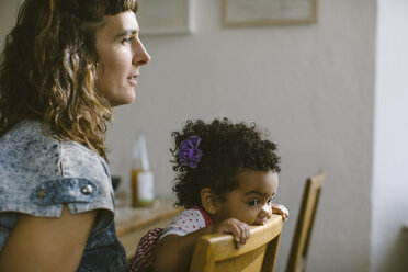 Seitenansicht der Mutter, die neben ihrer Tochter sitzt, die zu Hause in einen Stuhl beißt - MASF10796