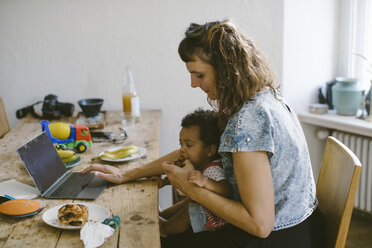 Woman using feeding food to daughter while sitting at dining table in house - MASF10799