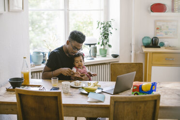 Young man playing with daughter while sitting at table in house - MASF10806