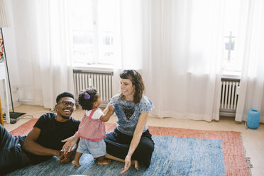 Happy mother and father with daughter on carpet at home - MASF10817