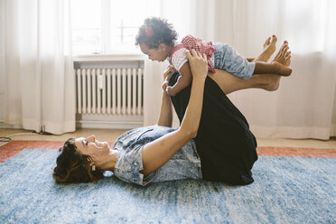 Playful mother lifting daughter while lying on carpet at home - MASF10819