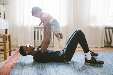 Playful father lifting daughter while lying on carpet at home - MASF10821