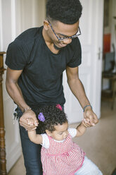 Smiling father assisting daughter in walking at home - MASF10824