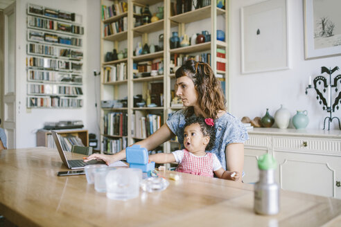 Frau benutzt Laptop, während sie mit ihrer Tochter am Esstisch im Haus sitzt - MASF10829
