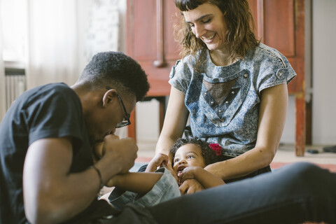 Vater küsst den Fuß der Tochter, die zu Hause auf dem Schoß der Mutter liegt, lizenzfreies Stockfoto