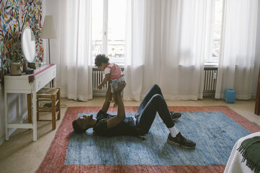 Verspielter Vater hebt Tochter hoch, während sie zu Hause auf dem Teppich liegt - MASF10841