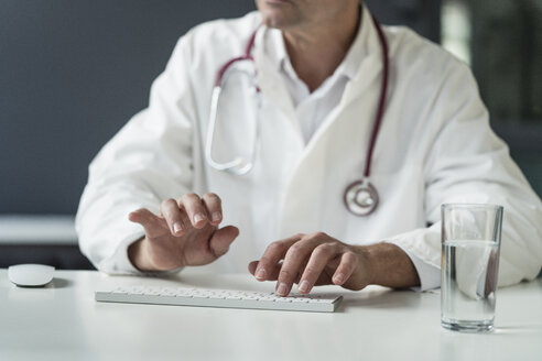 Close-up of doctor in medical practice typing on keyboard at desk - JOSF02774