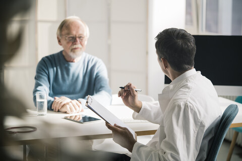 Arzt im Gespräch mit einem älteren Patienten in einer Arztpraxis, lizenzfreies Stockfoto