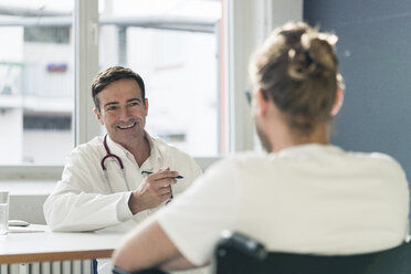 Lächelnder Arzt im Gespräch mit einem Patienten im Rollstuhl in einer Arztpraxis - JOSF02778
