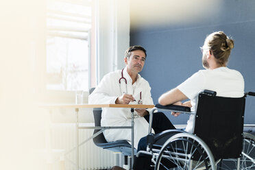 Arzt hört einem Patienten im Rollstuhl in einer Arztpraxis zu - JOSF02780
