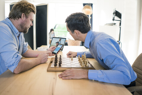 Zwei Männer spielen Schach und überprüfen ihr Smartphone, lizenzfreies Stockfoto