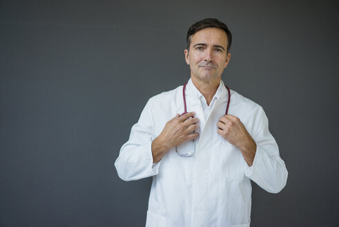 Portrait of confident doctor standing at a grey wall - JOSF02840