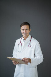 Porträt eines selbstbewussten Arztes, der ein Klemmbrett vor einer grauen Wand hält - JOSF02842