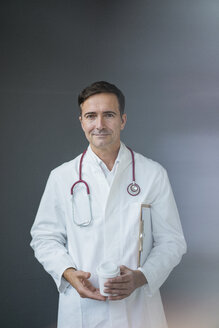 Portrait of confident doctor holding cup at a grey wall - JOSF02843