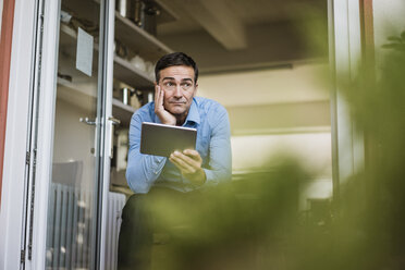 Businessman with tablet sitting at open French door - JOSF02851