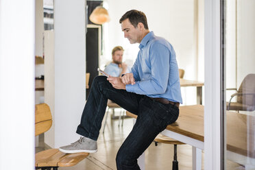 Businessman sitting on table using tablet - JOSF02856