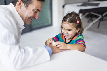 Doctor with plaster and happy girl at desk in medical practice - JOSF02860