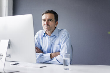 Serious businessman sitting at desk in office looking at computer screen - JOSF02861