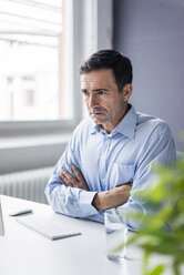 Serious businessman sitting at desk in office - JOSF02862