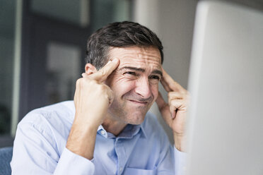 Grimassen schneidender Geschäftsmann mit Blick auf den Computerbildschirm - JOSF02863