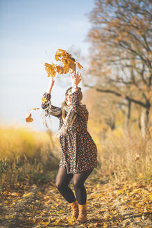 Happy pregnant woman standing on forest path playing with autumn leaves - ASCF00923