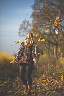 Happy pregnant woman standing on forest path playing with autumn leaves - ASCF00924