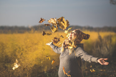 Glückliche schwangere Frau spielt mit Herbstblättern in der Natur - ASCF00925