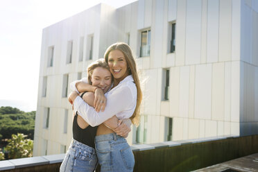 Girlfriends on a rooftop terrace, embracing by the pool - VABF02107