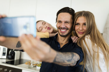 Friends having fun standing in the kitchen, taking pictures with their smartphones - VABF02166