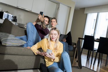 Freunde sitzen auf der Couch im Wohnzimmer und benutzen digitale Geräte - VABF02179