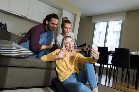 Friends sitting on couch in livingroom, using smartphone, chatting stock photo