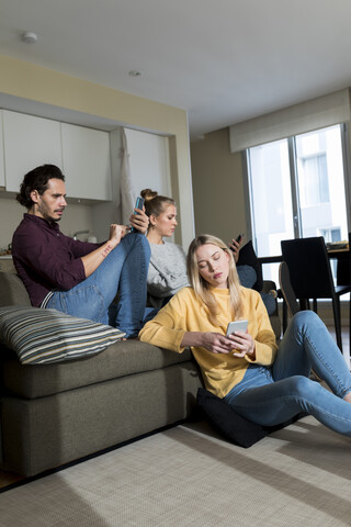 Gelangweilte Freunde sitzen auf der Couch im Wohnzimmer und benutzen digitale Geräte, lizenzfreies Stockfoto