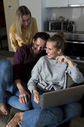 Freunde sitzen auf der Couch im Wohnzimmer, haben Spaß und benutzen einen Laptop - VABF02186