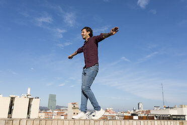 Mann auf einer Dachterrasse, auf einer Mauer balancierend - VABF02208