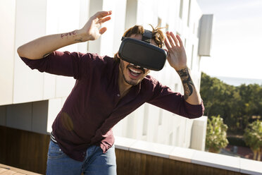 Man on a rooftop terrace, gaming with VR glasses - VABF02216