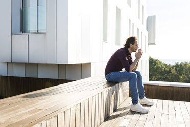 Man sitting on a rooftop terrace, looking worried - VABF02218