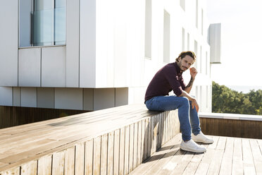 Man sitting on a rooftop terrace, looking worried - VABF02219