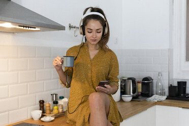 Young woman listening musuc in the kitchen, while drinking her morning coffee - ERRF00613